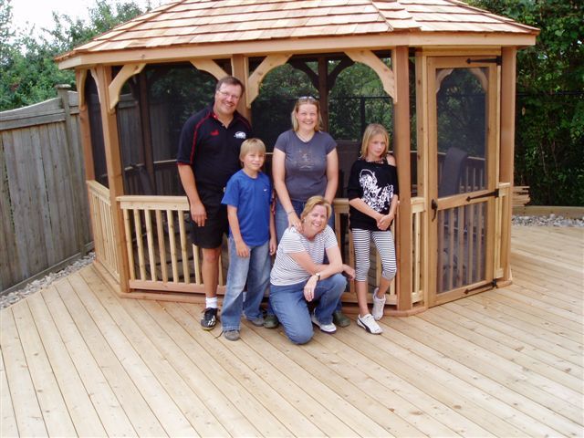 wooden 10 by 14 foot oval gazebo with happy family standing in front